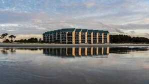 Hotel com vários andares e piscina refletora em frente, localizado perto de uma praia.