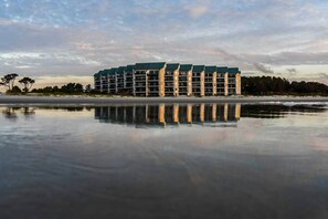 Ein mehrstöckiges Hotel mit einem spiegelnden Pool davor, in Strandnähe gelegen.