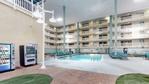 Una piscina interior con varios niveles de balcones, máquinas expendedoras y una zona junto a la piscina con tumbonas.