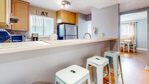 Una cocina con mostrador, refrigerador, armarios y una ventana con persianas.