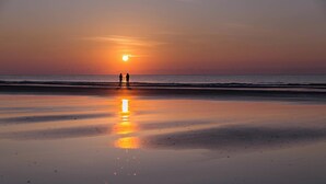 A beach scene with two people standing at the water's edge during sunset. - Spacious, Renovated House with Private Spa and Private Pool (Hilton Head)