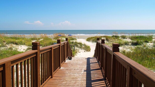 Een houten looppad dat naar een strand met duinen en de oceaan in de verte leidt.