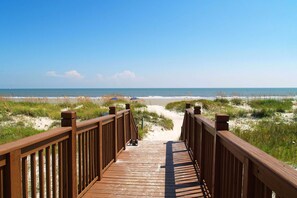 A wooden boardwalk leading to a beach with sand dunes and the ocean in the background. - A spacious condo with community pool, hot tub, and oceanfront views (Hilton Head)