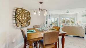 Een eethoek met een houten tafel, stoelen, een kroonluchter en een wandkunstwerk van geweven materiaal.