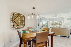 A dining area with a wooden table, chairs, a chandelier, and a woven wall art piece. - A spacious condo with community pool, hot tub, and oceanfront views (Hilton Head)