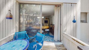 Un patio con puerta de vidrio que da a un comedor interior, sillas azules y una alfombra estampada.