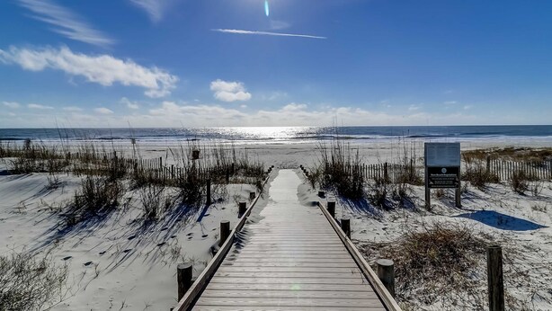 Pasarela de madera que conduce a una playa, cielo despejado y un cartel que indica zona de normativa de playa.