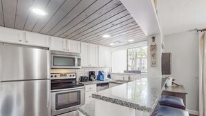 Una cocina moderna con electrodomésticos de acero inoxidable, encimera de granito y barra con taburetes.