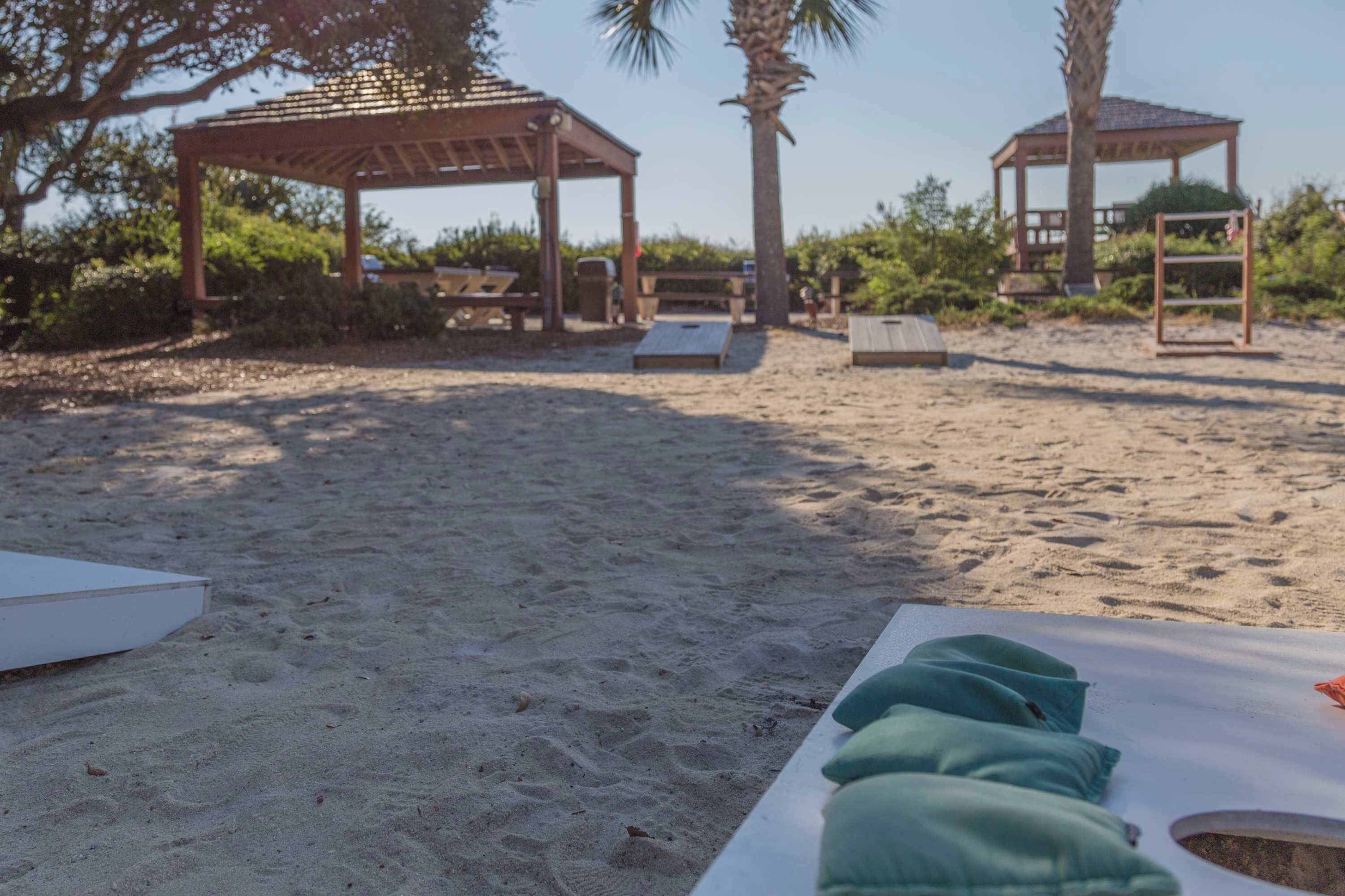 Eine Strandlandschaft mit Holzkiosken, Picknicktischen und einer weißen Lounge-Bereich mit grünen Kissen.