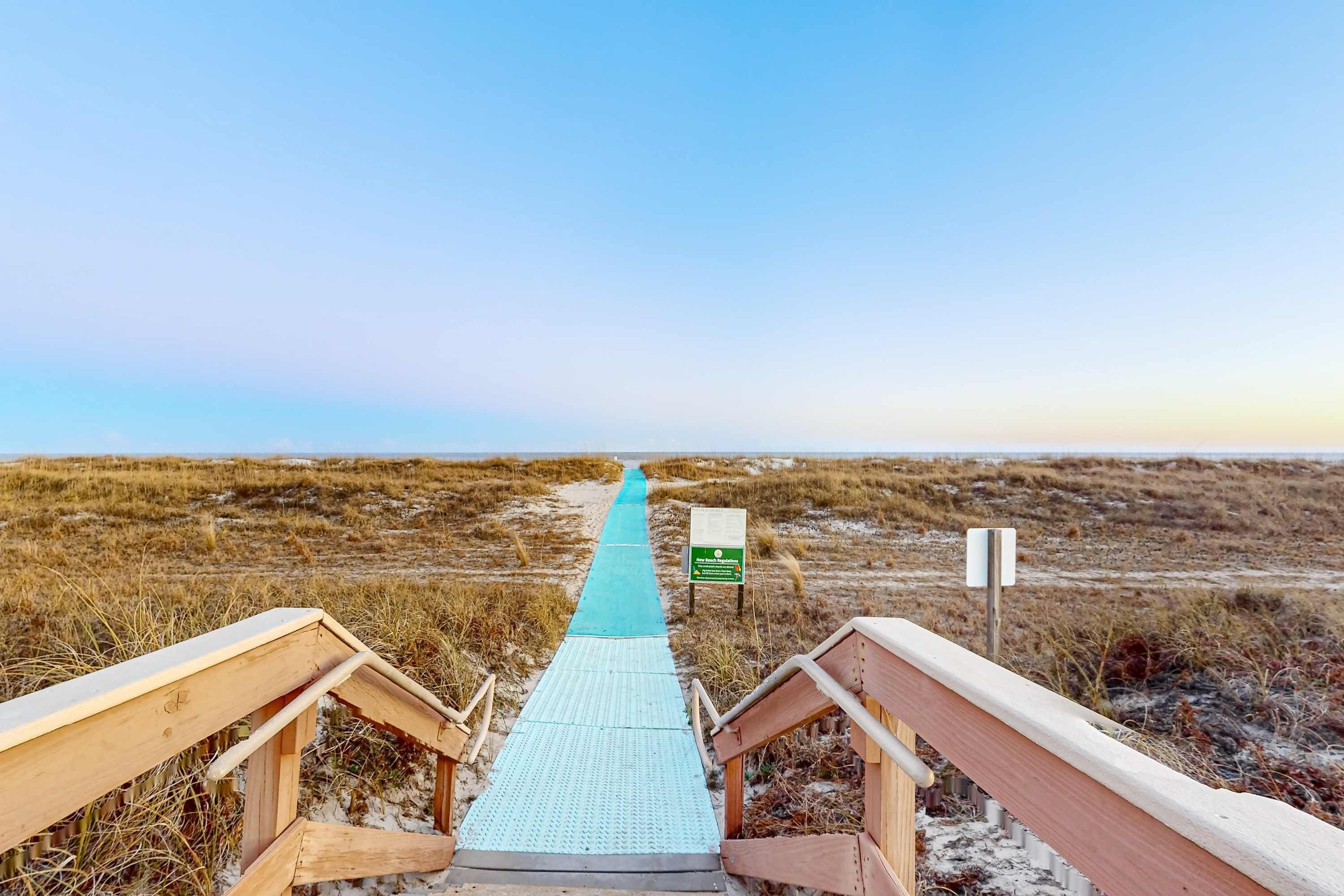 Une promenade en bois qui mène à une plage, avec un ciel dégagé.