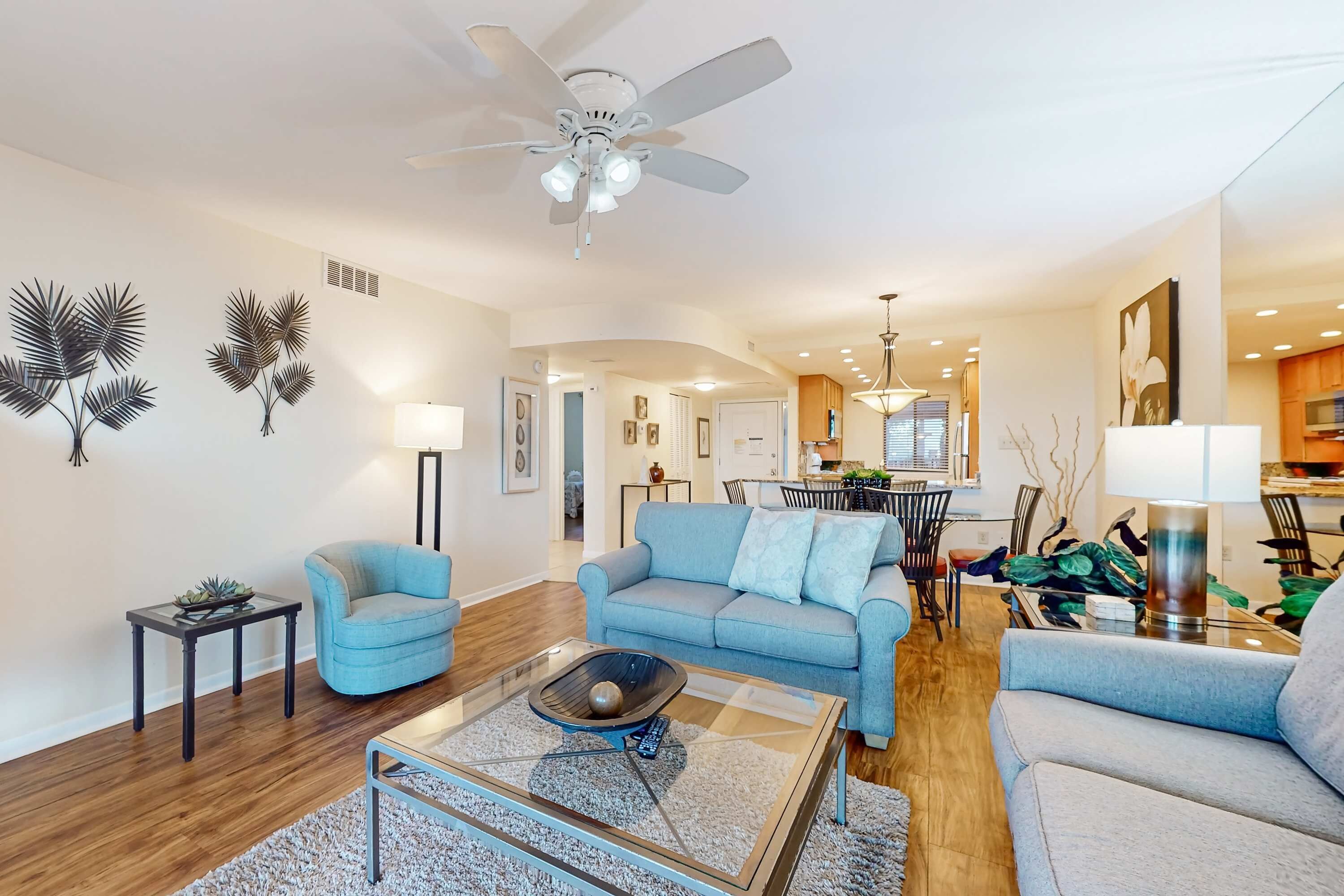 Ein modernes Wohnzimmer mit Deckenventilator, zwei Sofas, einem Couchtisch und einem Essbereich im Hintergrund.