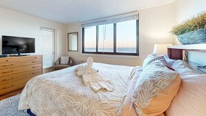 Un dormitorio con cama, televisor, cómoda, ventana y planta.