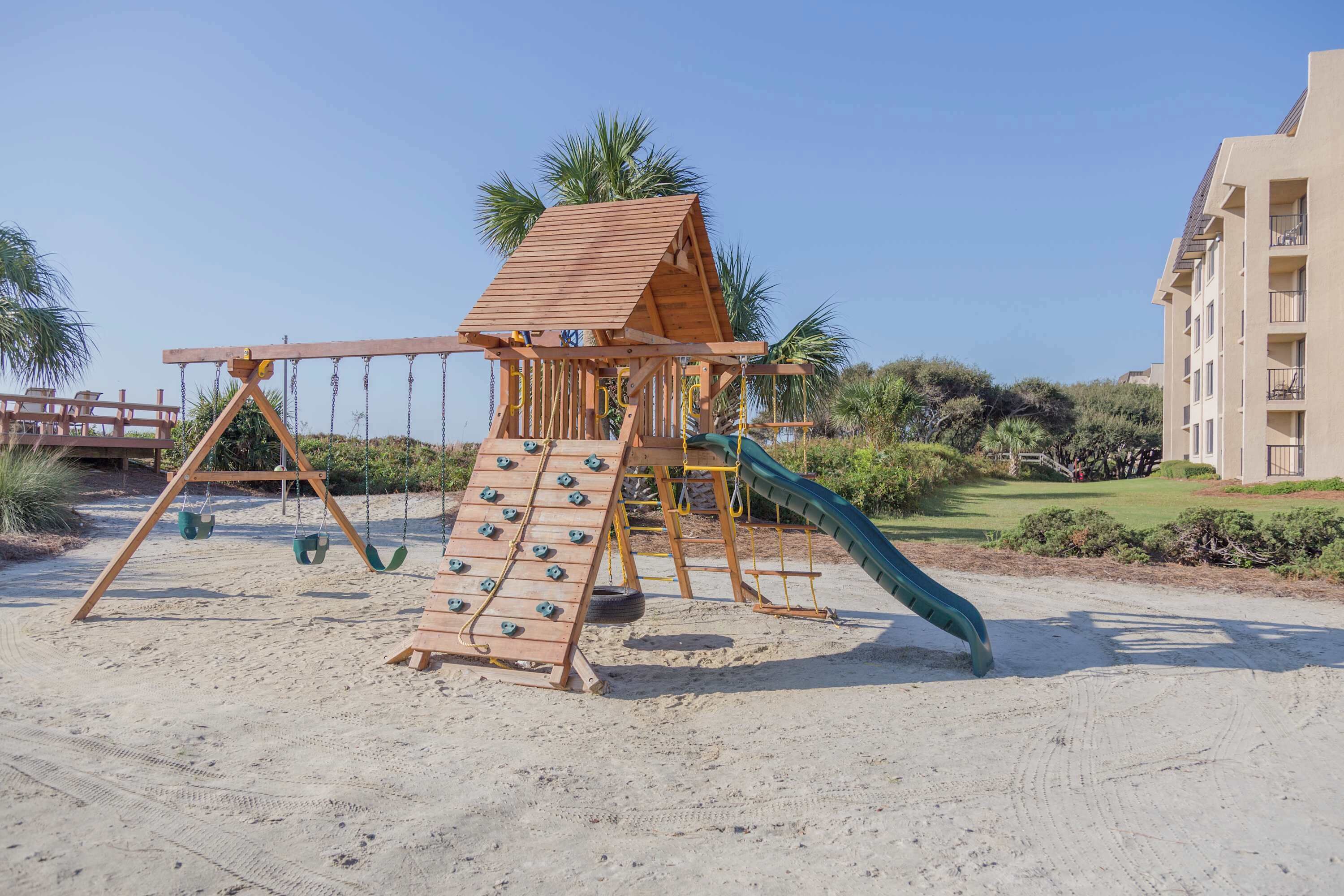 A wooden playground structure with a slide, swings, and climbing area.