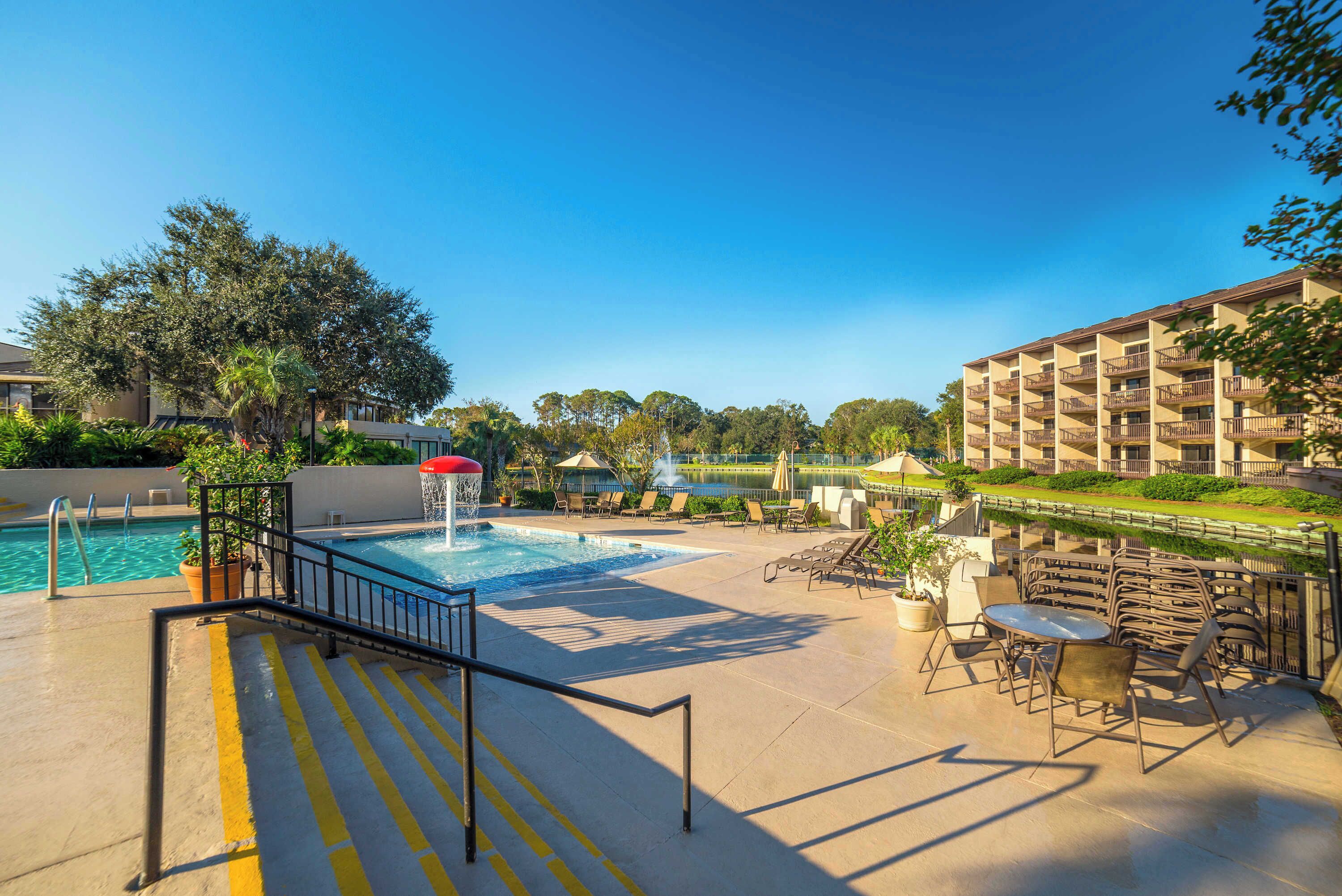 A pool area with a water feature, lounge chairs, and a building with balconies.