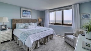 Un dormitorio con cama, mesitas de noche, un sofá, una ventana con vistas y una planta en maceta.