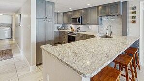 Una cocina moderna con encimeras de granito, electrodomésticos de acero inoxidable y taburetes de bar.