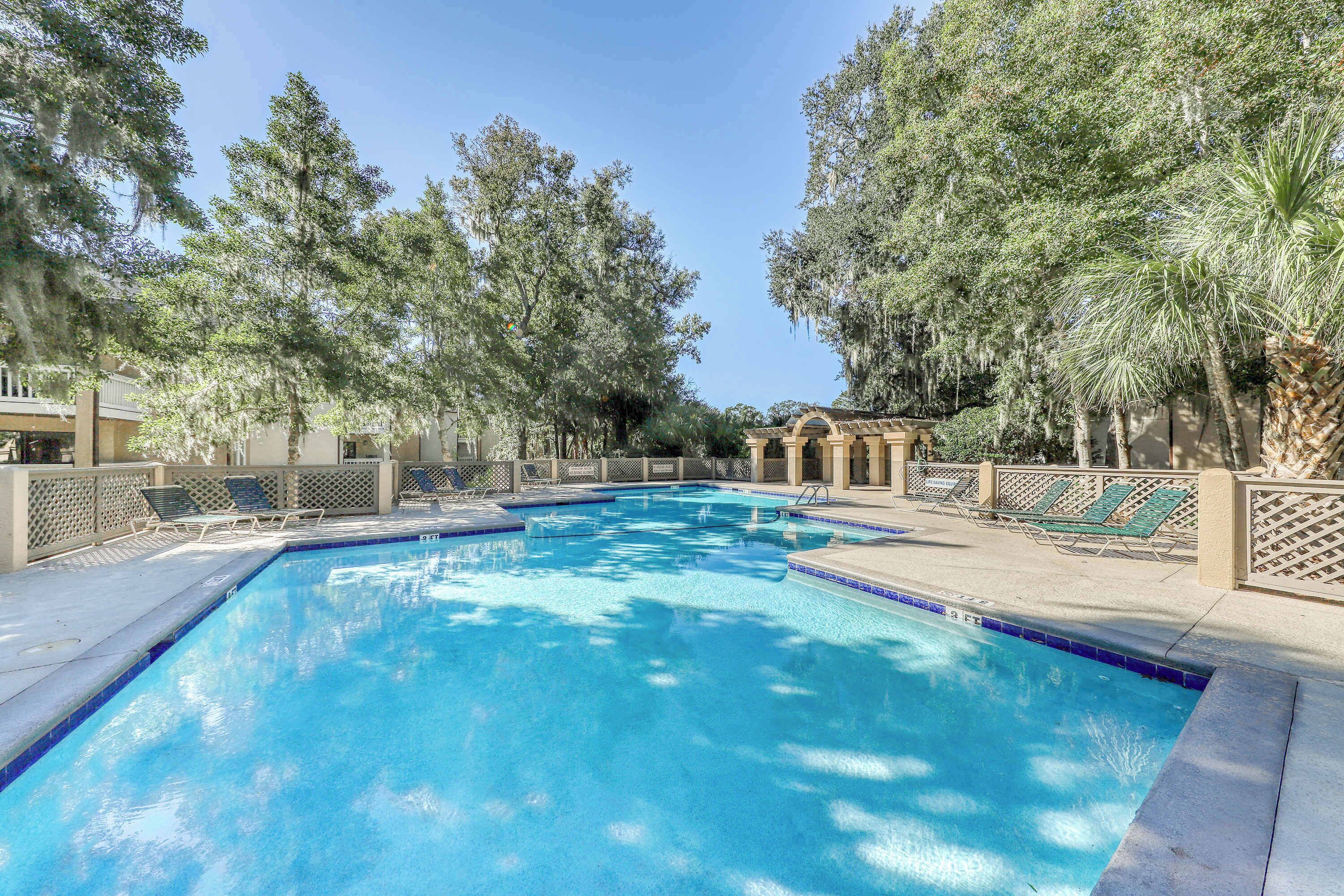 Una piscina con bordo piastrellato, circondata da alberi e lettini.