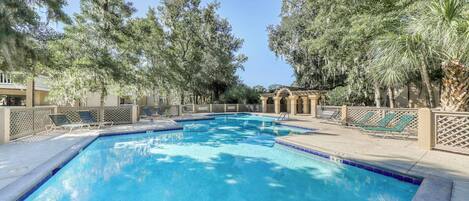 Una piscina con bordo piastrellato, circondata da alberi e lettini.