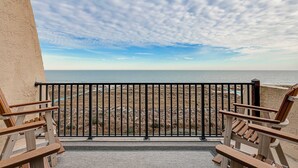 A balcony with a view of the beach, wooden chairs, and a black metal railing. - Charming Waterfront Getaway with Seasonal Pool & Hot Tub, Tennis, Beach Access (Hilton Head)