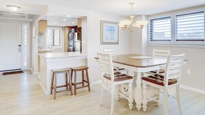 Uma sala de jantar com mesa de madeira, cadeiras brancas e lustre.