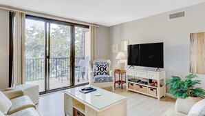 Uma sala de estar moderna com sofá, mesa de centro, televisão, poltrona, luminária e varanda com mobiliário externo.