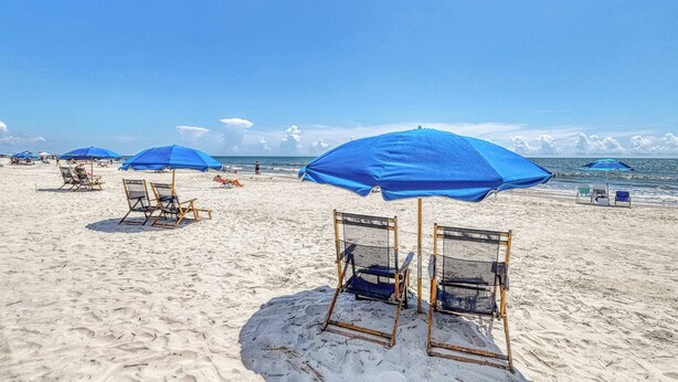 Uma praia com guarda-sóis azuis e cadeiras de praia.