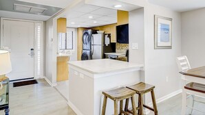 Uma cozinha moderna com uma ilha central, banquetas de madeira e uma área de jantar com mesa e cadeiras brancas.