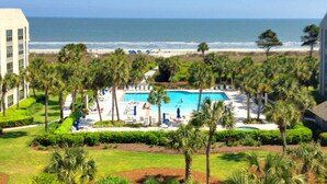 A resort with a pool, palm trees, and a beach view. - Resort Condo with Al Fresco Dining, Shared Pool, Hot Tub & Beach Access (Hilton Head)