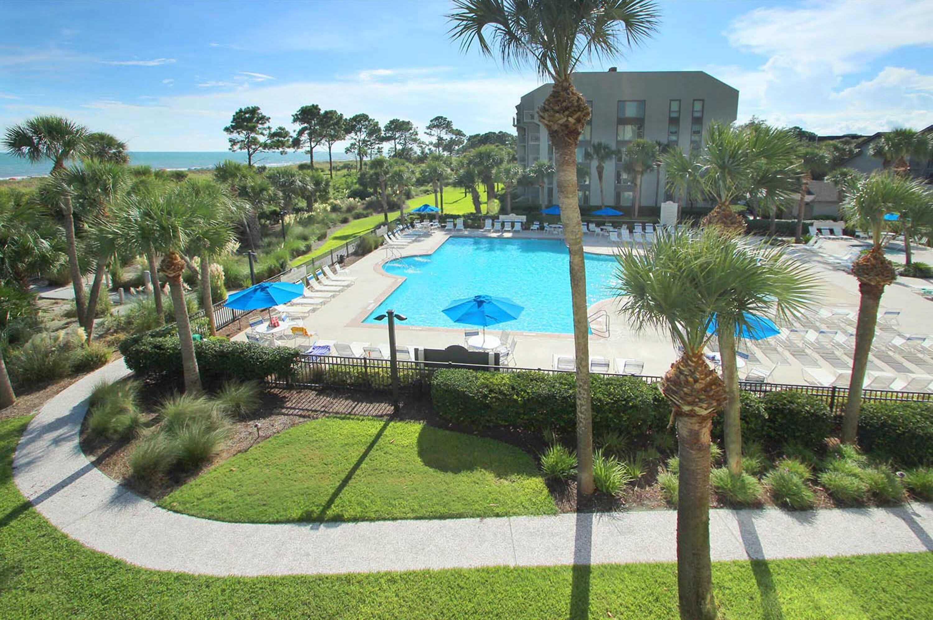 A resort pool area with palm trees, a large pool, and a building in the background.