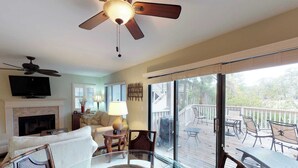 Un salon doté d’une cheminée, d’un téléviseur, d’un ventilateur de plafond et d’une porte vitrée donnant sur une terrasse extérieure.