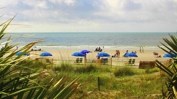 Une plage avec des parasols et des chaises, une clôture et l’océan.