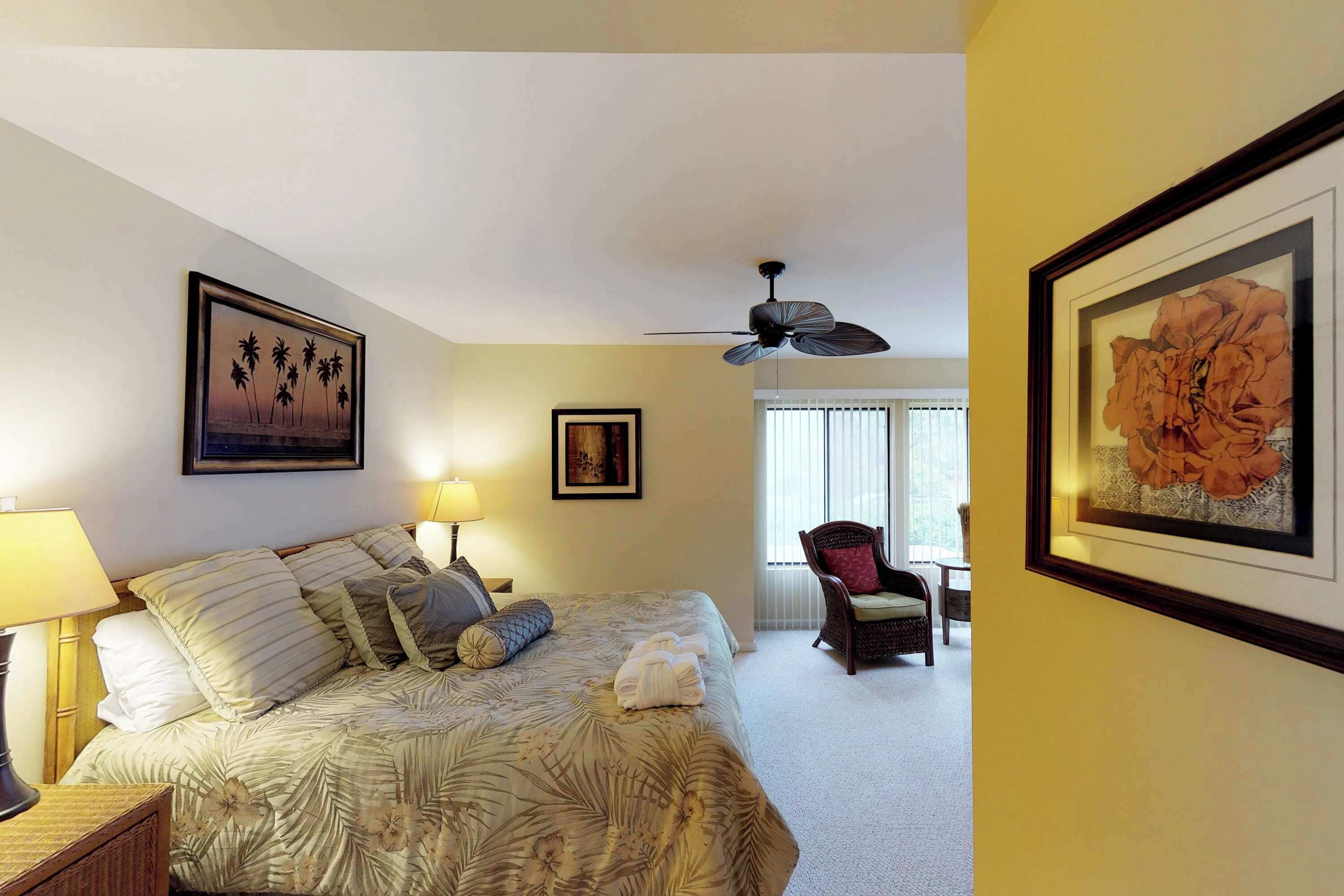 A hotel room with a bed, a ceiling fan, a chair, and artwork on the walls.