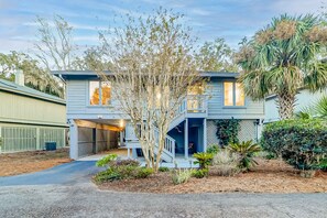 A two-story house with a covered garage, a small porch, and a landscaped garden with various plants and a palm tree. - Enchanting beach golf retreat with pool, screened porch & amazing views (Hilton Head)