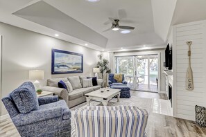 A living room with a sofa, armchair, ottoman, coffee table, and a painting on the wall. - Enchanting beach golf retreat with pool, screened porch & amazing views (Hilton Head)