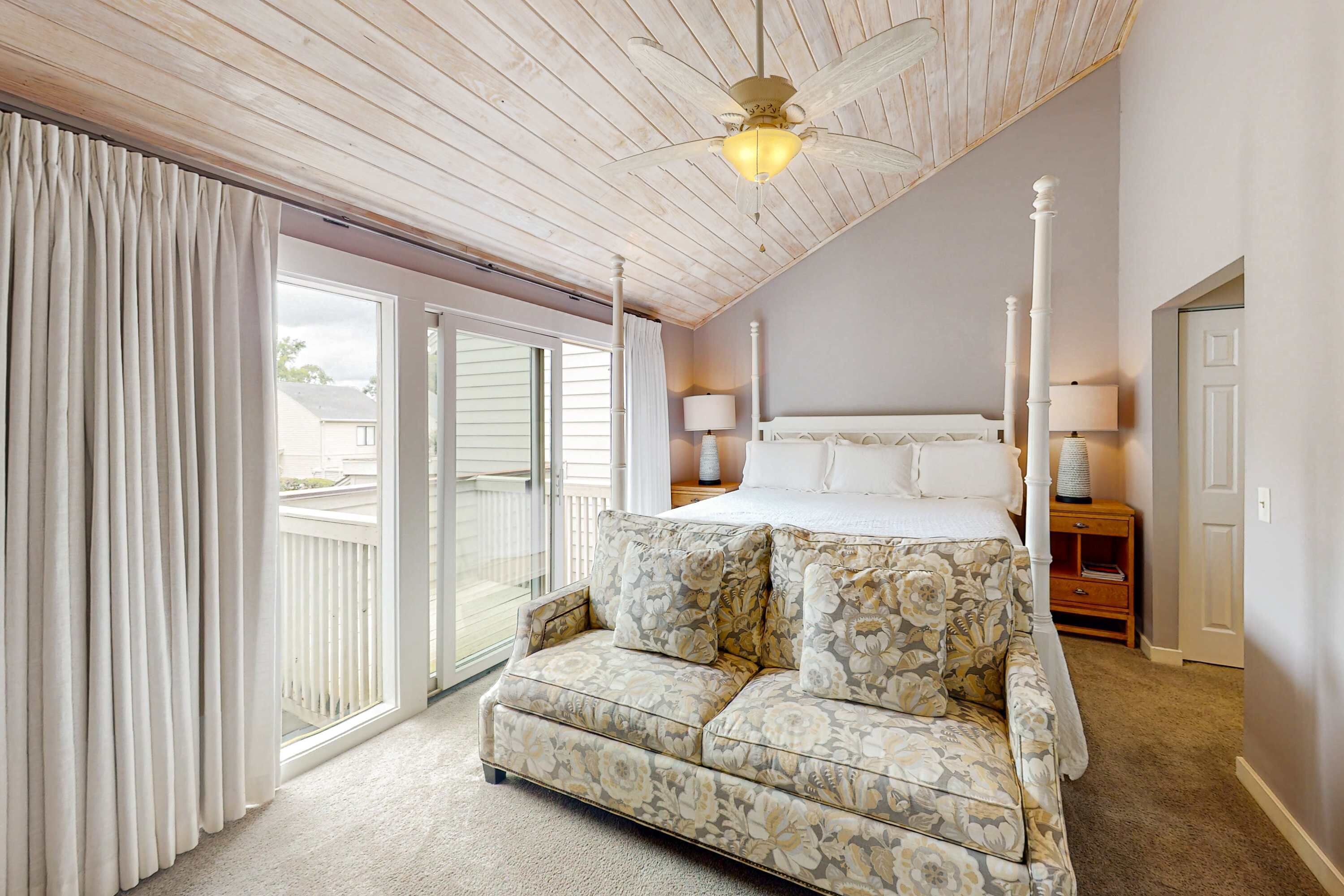 A bedroom with a bed, a nightstand, a lamp, a ceiling fan, and a sliding glass door to the outside.