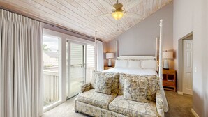 Quarto com cama, mesa de cabeceira, luminária, ventilador de teto e porta de vidro deslizante para o exterior.