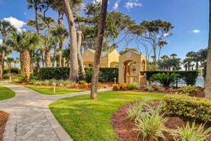 A pathway leading to a building with a symmetrical facade, surrounded by palm trees and well-maintained landscaping. - Oceanfront getaway with lagoon views, shared pool & hot tub, walk to beach (Hilton Head)