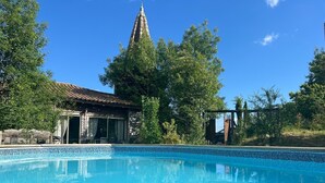 En swimmingpool med en kant som är klädd med kakel, en byggnad med ett tak som är täckt med kakel, och träd i bakgrunden.