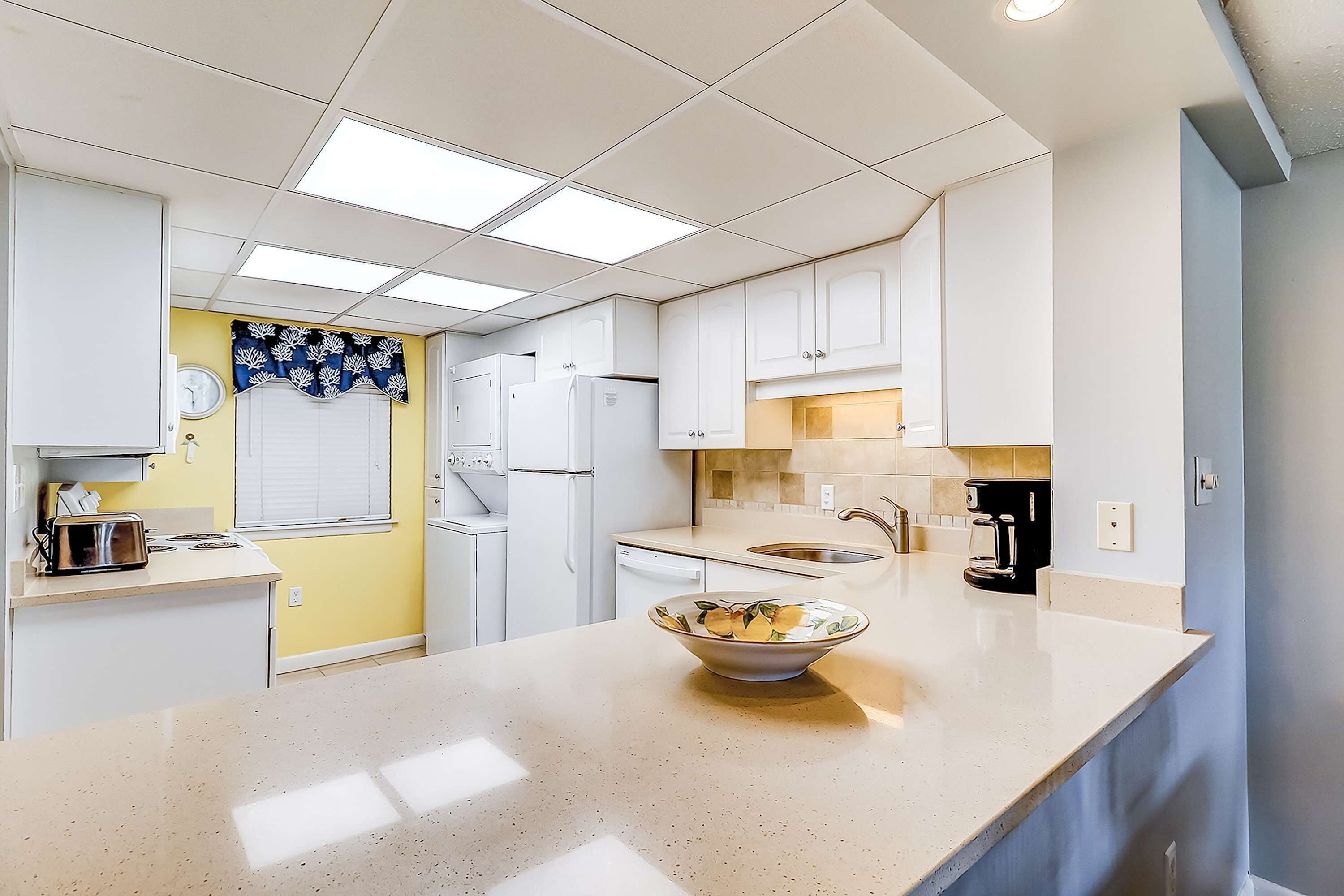 A kitchen with white cabinets, a countertop with a bowl, a refrigerator, a sink, and a window with blinds.