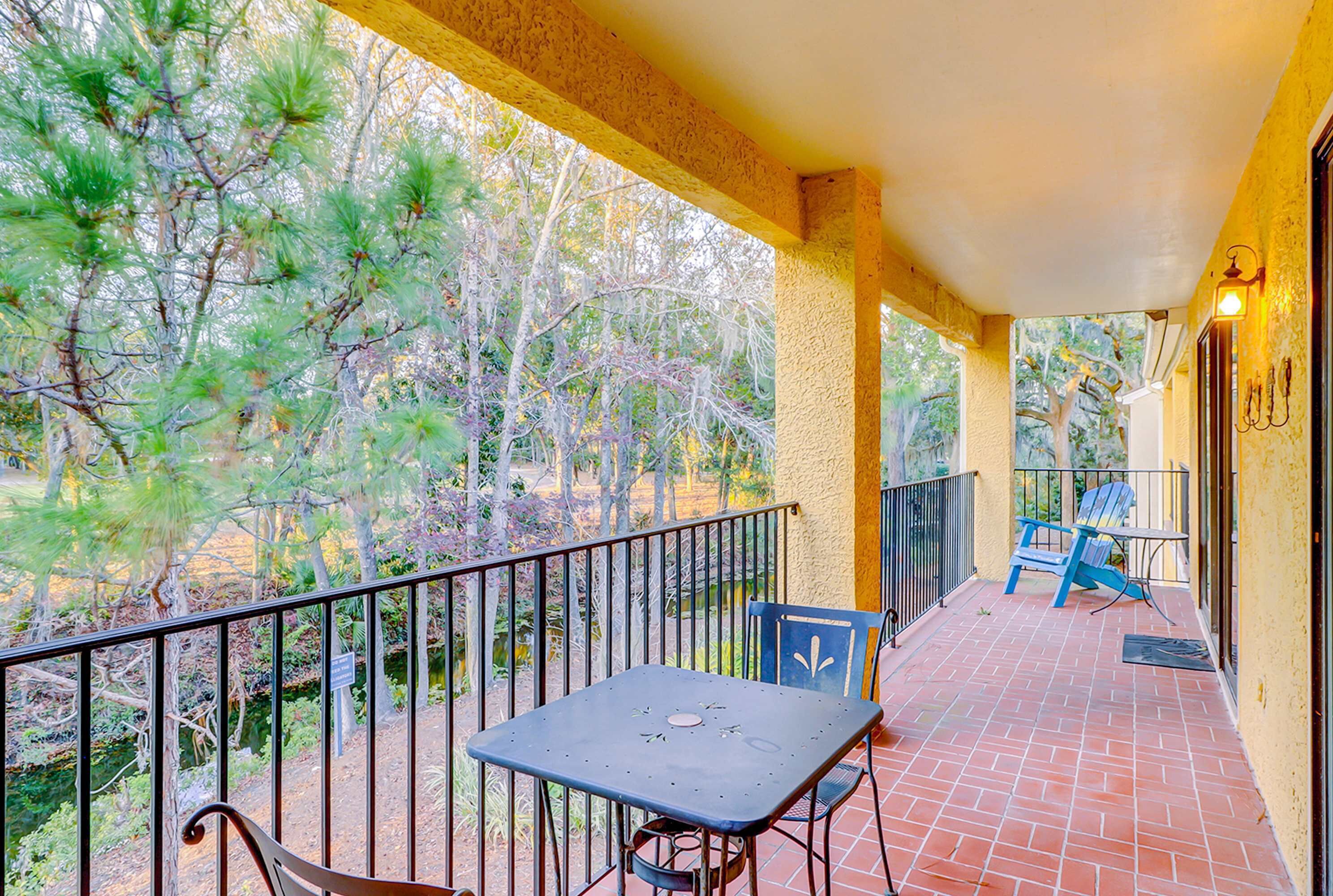 A balcony with a table and chairs, a railing, and a view of trees.