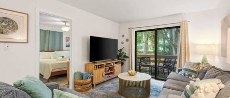 A living room with a sofa, TV, and a view of the outdoors.