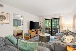 A living room with a sofa, TV, and a view of the outdoors. - Adorable 1st Floor Condo On site pool, tennis, pickle ball, near beach (Hilton Head)