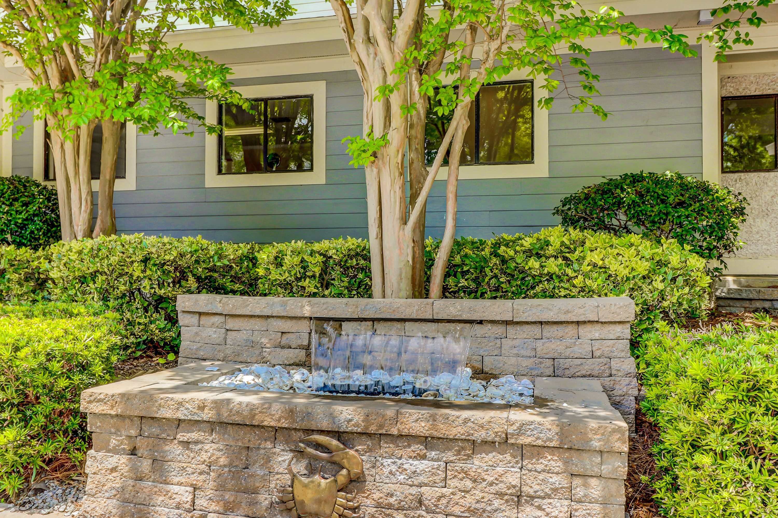 A stone fountain with water spouting from the center, surrounded by well-maintained hedges and trees. - Adorable 1st Floor Condo On site pool, tennis, pickle ball, near beach (Hilton Head)