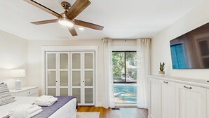 Ein Hotelzimmer mit einem Bett, einem Deckenventilator, einem Fernseher, einer Schiebetür zum Außenbereich und einem weißen Schrank.