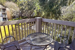 A wooden deck with a metal table and two chairs, overlooking a pond and surrounding trees. - Welcoming condo w pool, near beach & shopping plus balcony overlooking the lagoon (Hilton Head)