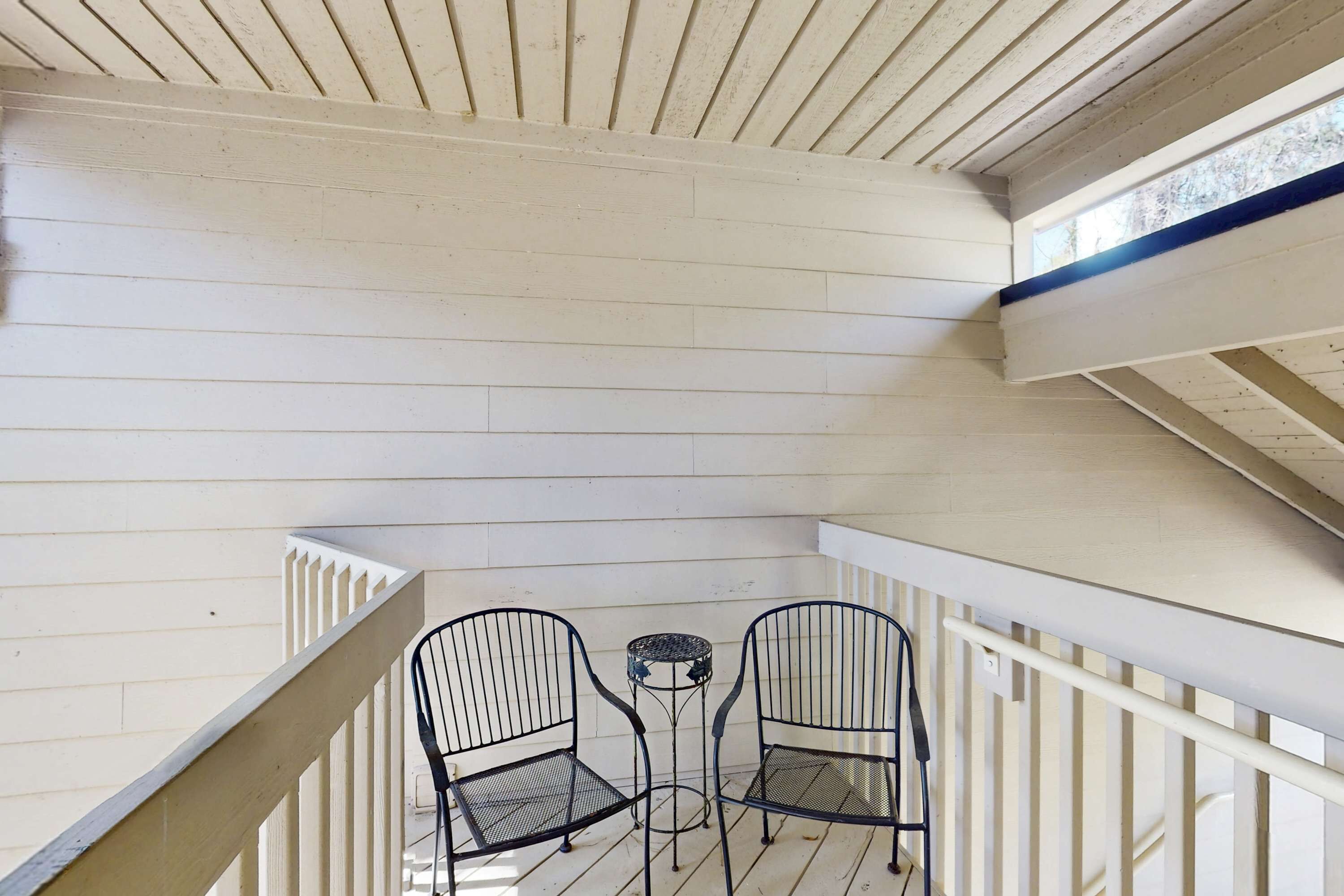 A balcony with white wooden railings, two metal chairs, and a small round table.