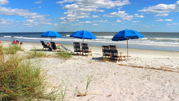A beach with blue umbrellas, lounge chairs, and a clear sky. - Palmetto Dunes condo with shared pool, private WD and beach access (Hilton Head)