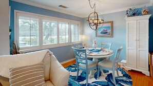 A dining area with a round table, chairs, a chandelier, and a large window with blinds. - Palmetto Dunes condo with shared pool, private WD and beach access (Hilton Head)