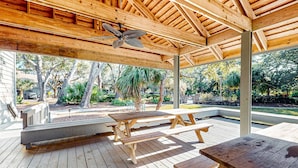 A covered outdoor area with wooden picnic tables and benches, a ceiling fan, and a view of a landscaped garden. - Palmetto Dunes condo with shared pool, private WD and beach access (Hilton Head)