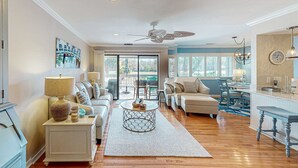 A spacious living room with a sofa, a coffee table, and a dining area with a chandelier. - Palmetto Dunes condo with shared pool, private WD and beach access (Hilton Head)